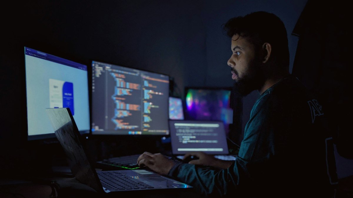 Photo by Abu Saeid on Unsplash. Source: https://unsplash.com/photos/a-man-sitting-in-front-of-three-computer-monitors-fdGTi4IcaJc (Unsplash License).