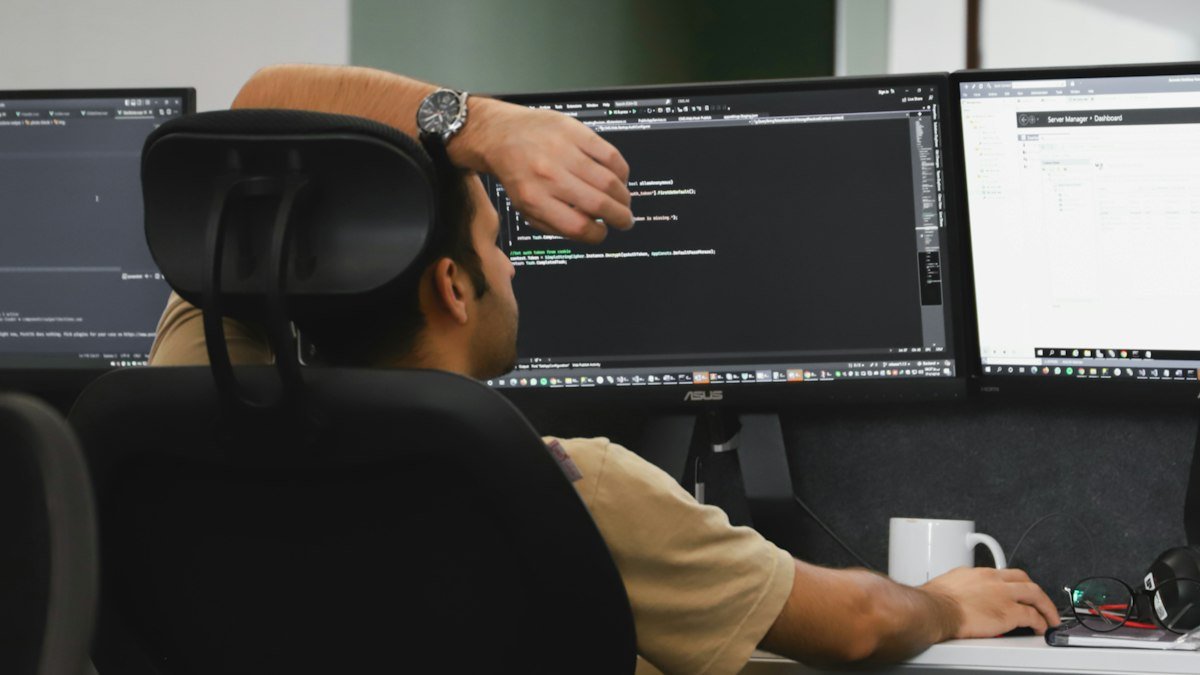 Photo by Fatemeh Rezvani on Unsplash. Source: https://unsplash.com/photos/a-man-sitting-in-front-of-two-computer-monitors-Xn3D8DIzH7Q (Unsplash License).