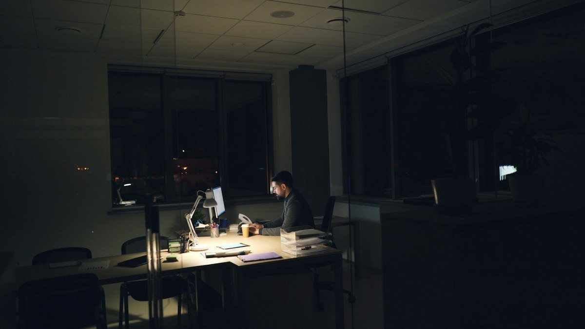 Photo by Vitaly Gariev on Unsplash. Source: https://unsplash.com/photos/man-working-late-at-a-dimly-lit-office-desk-l12wb6pAzuQ (Unsplash License). A man working alone in a dimly lit office at night.