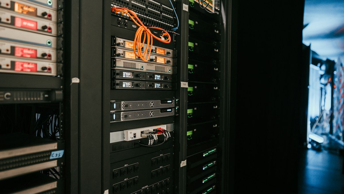 A rack of servers and network equipment in a data center aisle. Photo by Kevin Ache on Unsplash. Source: https://unsplash.com/photos/a-rack-of-servers-in-a-server-room-2JJ3wBHu4_0 (Unsplash License).