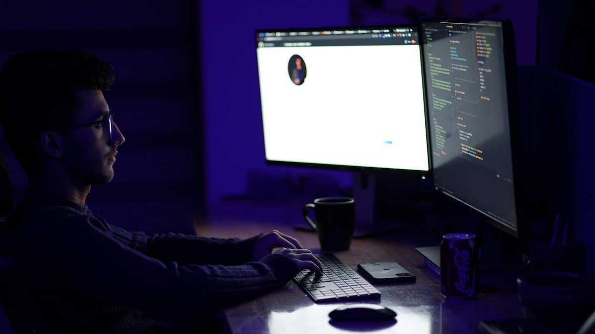 Photo by Mohammad Rahmani on Unsplash. Source: https://unsplash.com/photos/a-man-sitting-at-a-desk-in-front-of-a-computer-Wgw0wwXMdk0 (Unsplash License).