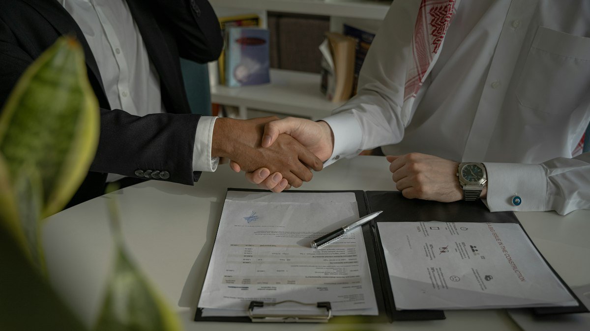 Photo by Amina Atar on Unsplash. Source: https://unsplash.com/photos/two-people-shaking-hands-over-a-piece-of-paper-4mEyvORkbN0 (Unsplash License).