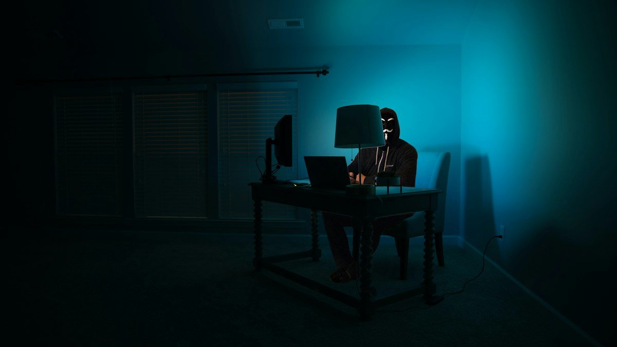A person working at a desk in a dark room. Photo by kartik programmer on Unsplash. Source: https://unsplash.com/photos/a-person-sitting-at-a-desk-in-a-dark-room-JrEHwkPIurA (Unsplash License).
