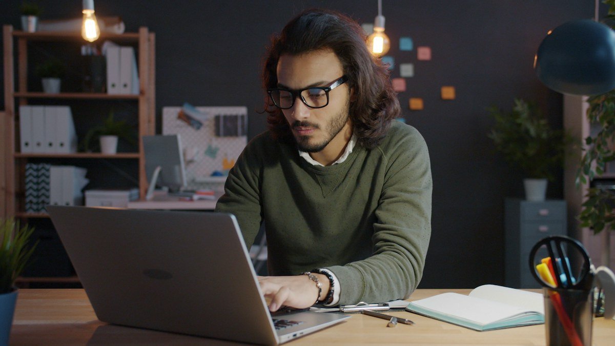 Photo by Vitaly Gariev on Unsplash. Source: https://unsplash.com/photos/man-working-on-laptop-in-dimly-lit-office-W8FvUgCLO6U (Unsplash License). A man working at a laptop in a dimly lit office at night.