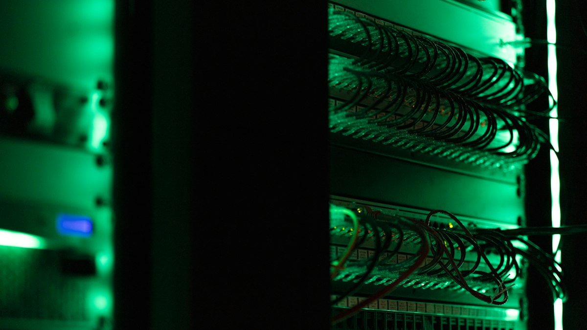 Photo by Tyler on Unsplash. Source: https://unsplash.com/photos/a-rack-of-electronic-equipment-in-a-dark-room-OnI_TNcIv9U (Unsplash License).
