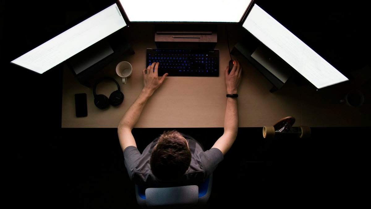 Photo by Max Duzij on Unsplash. Source: https://unsplash.com/photos/man-facing-three-computer-monitors-while-sitting-qAjJk-un3BI (Unsplash License).