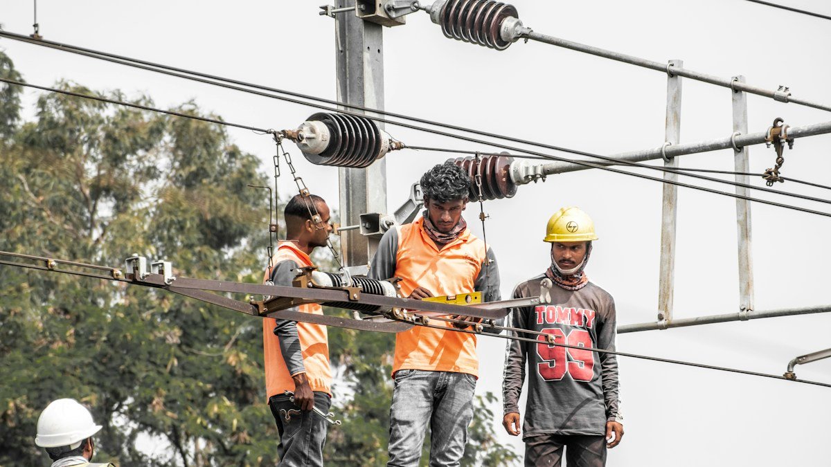 Photo by aboodi vesakaran on Unsplash. Source: https://unsplash.com/photos/a-group-of-men-standing-on-top-of-a-power-line-kMlpYZh2KsI (Unsplash License).