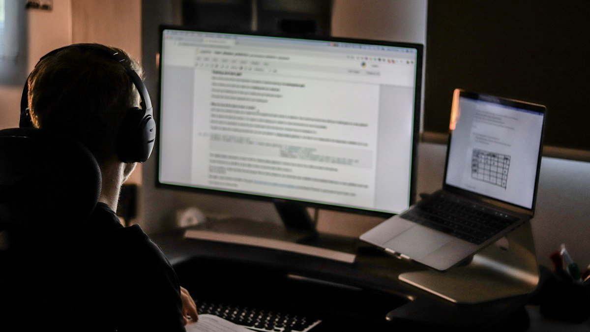 Photo by Samuel Bourke on Unsplash. Source: https://unsplash.com/photos/sc-B_2-Om7Q (Unsplash License). A developer in headphones works through the night at two screens.
