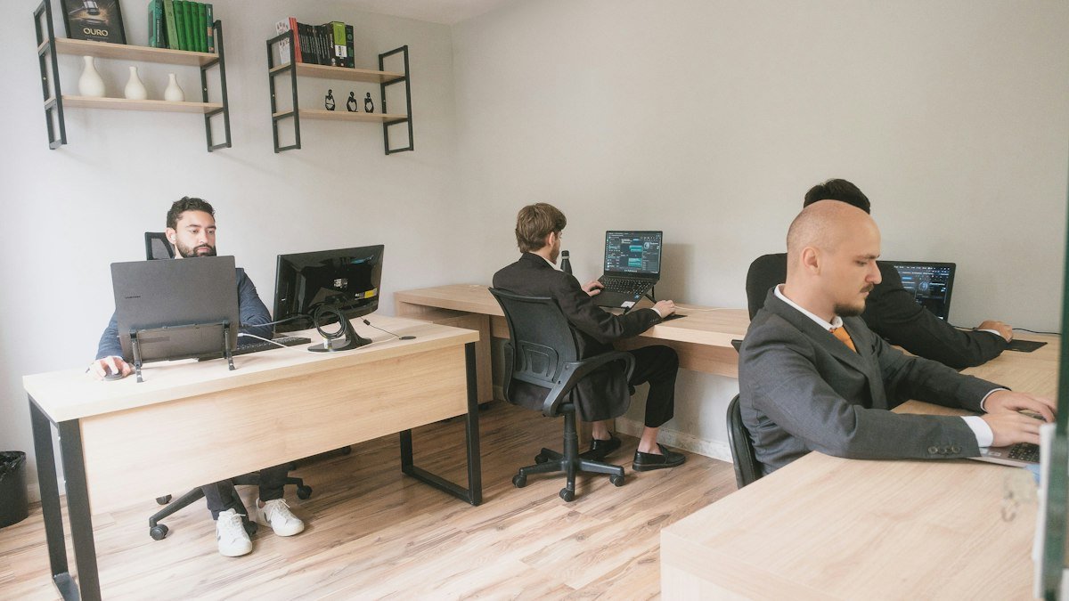 Photo by Joao Victor da Silva Ribeiro on Unsplash. Source: https://unsplash.com/photos/EcEp6_kYyYM (Unsplash License). Four people in office dress working at laptops and monitors in a shared workspace.