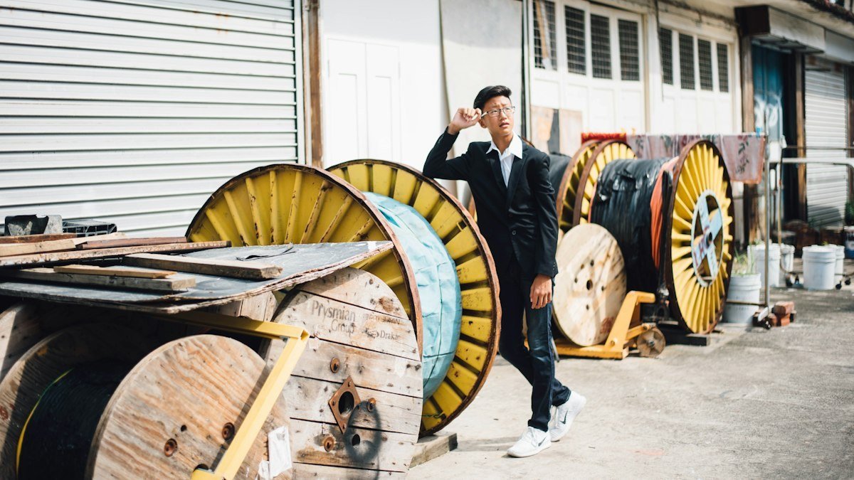 Cable reels stacked beside a warehouse where workers prepare outside plant cable. Photo by CHUTTERSNAP on Unsplash. Source: https://unsplash.com/photos/man-standing-beside-spool-of-cable-cRqnRyNOy4w (Unsplash License).