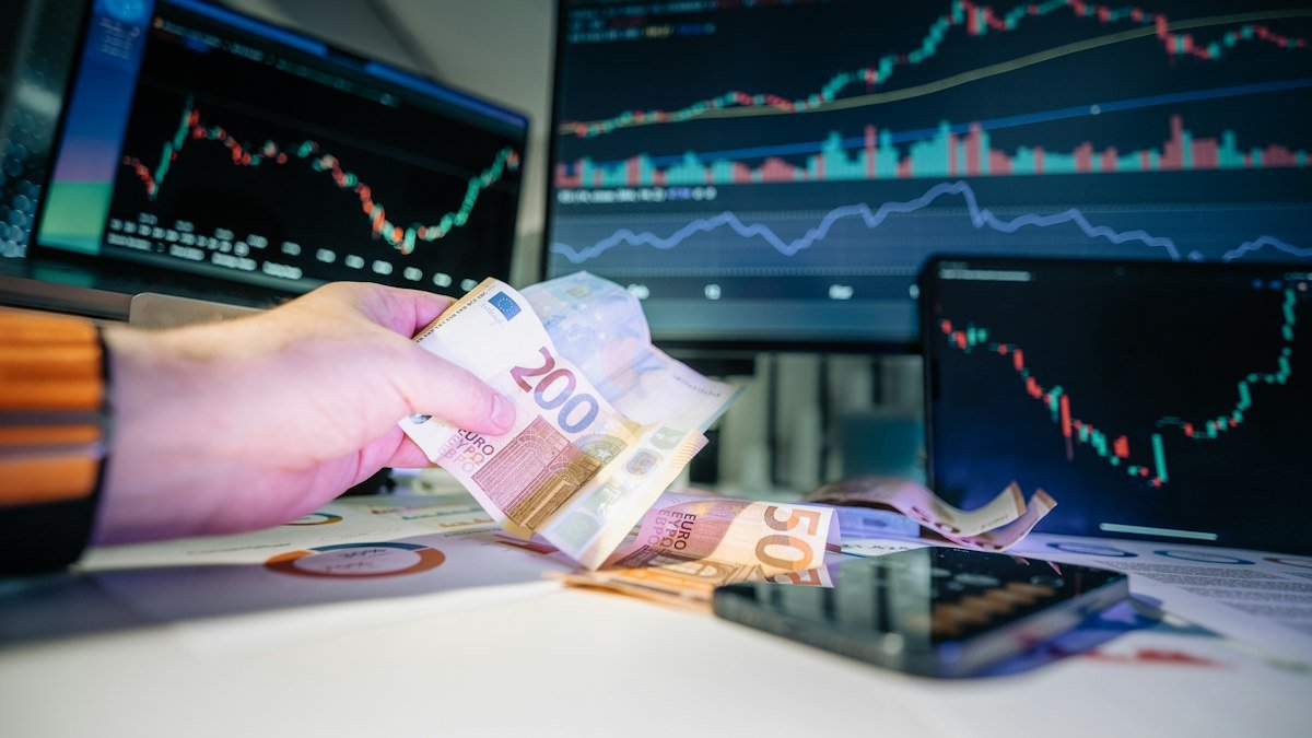 Photo by Jakub Żerdzicki on Unsplash. Source: https://unsplash.com/photos/a-person-holding-money-in-front-of-a-computer-screen-TUmKOI0bK-w (Unsplash License).