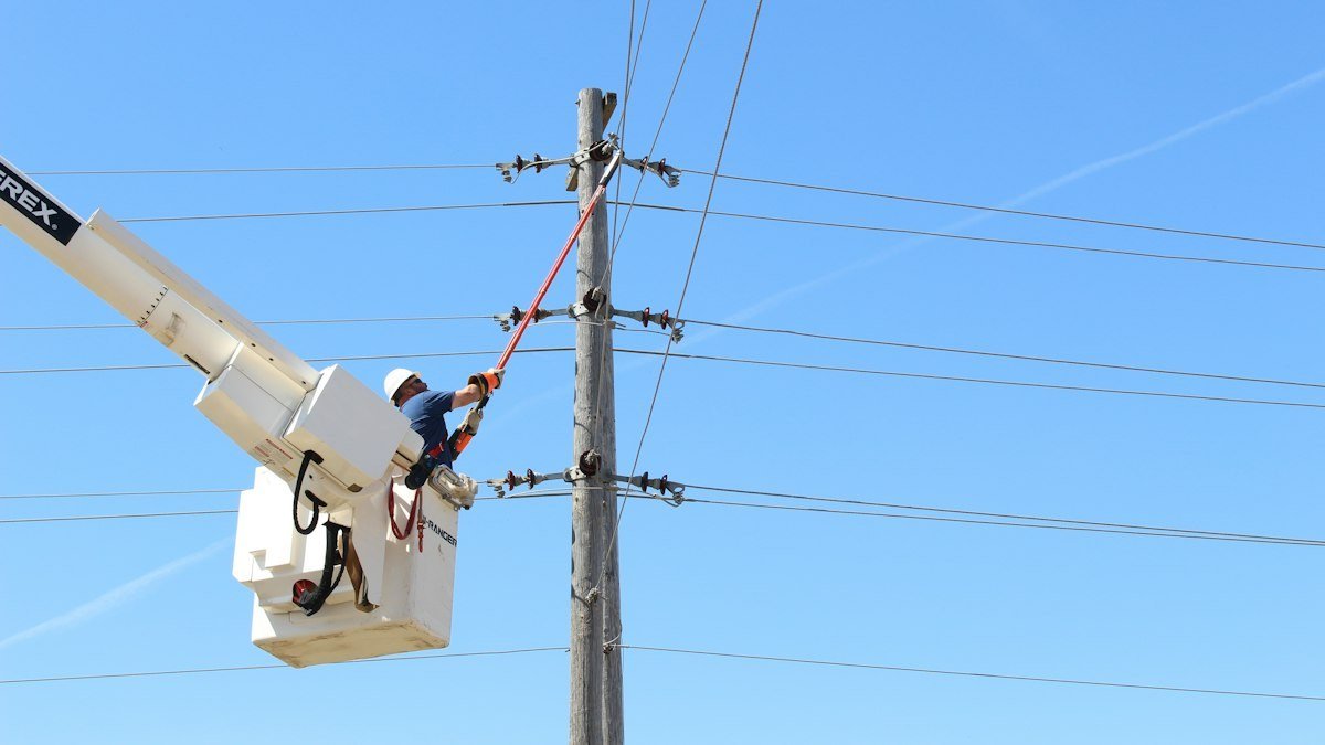 A lineworker in a bucket truck works on overhead power lines. Photo by American Public Power Association on Unsplash. Source: https://unsplash.com/photos/man-holding-stick-near-transmission-tower-uxH3GL1T0lI (Unsplash License).