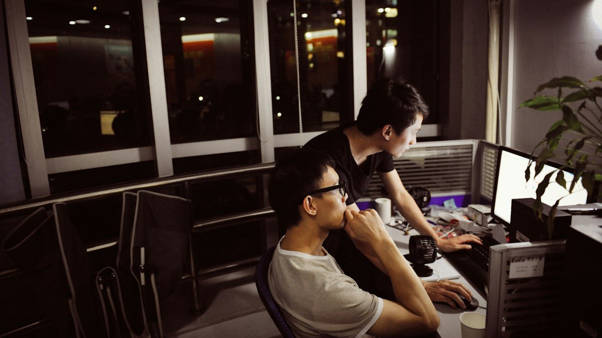 Two engineers working at monitors late at night. Photo by blue sky on Unsplash. Source: https://unsplash.com/photos/QN1Sz74hVjg (Unsplash License).