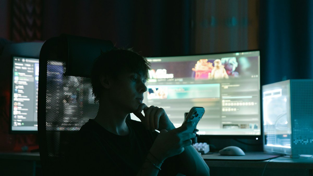 Photo by Mikhail Pushkarev on Unsplash. Source: https://unsplash.com/photos/person-looking-at-phone-in-front-of-multiple-computer-monitors-VhhlVXFaJXs (Unsplash License).