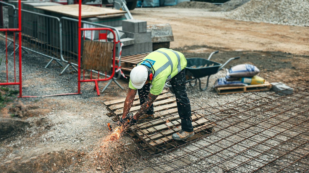 Photo by Emma Houghton on Unsplash. Source: https://unsplash.com/photos/man-in-green-and-yellow-safety-vest-and-blue-denim-jeans-standing-on-brown-wooden-pallet-EixJzIdl4bc (Unsplash License).