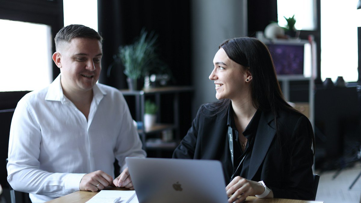 Photo by Lyubomyr Reverchuk on Unsplash. Source: https://unsplash.com/photos/a-man-and-a-woman-sitting-at-a-table-with-a-laptop-CvyRP10doo0 (Unsplash License).